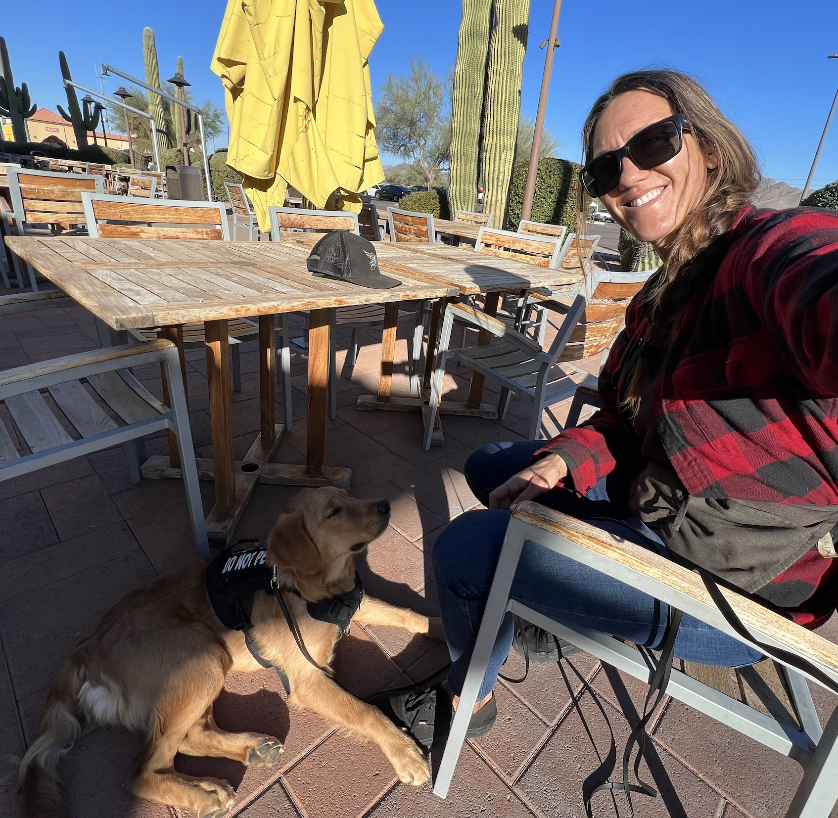 Active K9 trainer sitting at an outdoor cafe with a service dog lying calmly on the ground.